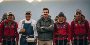 A smiling and professional Inca Trail team, including a guide, chef, and porters, standing together in the Andean mountains of Peru.