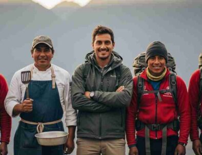 A smiling and professional Inca Trail team, including a guide, chef, and porters, standing together in the Andean mountains of Peru.