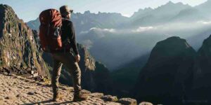 A hiker pauses on an ancient Inca stone path looking out at the Andes mountains during high-altitude trekking.